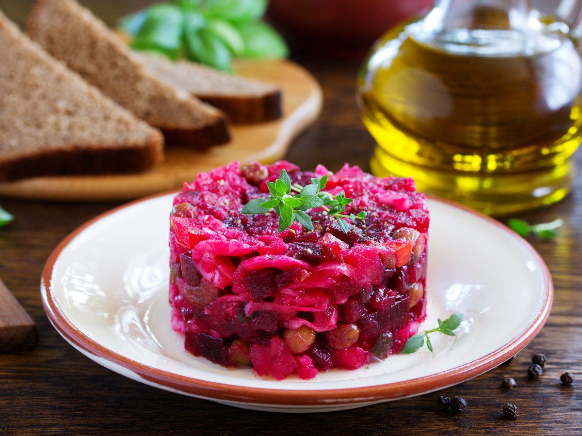 Rote-Bete-Tatar auf einem weißen Teller, dahinter eine Flasche Öl und Brotscheiben.