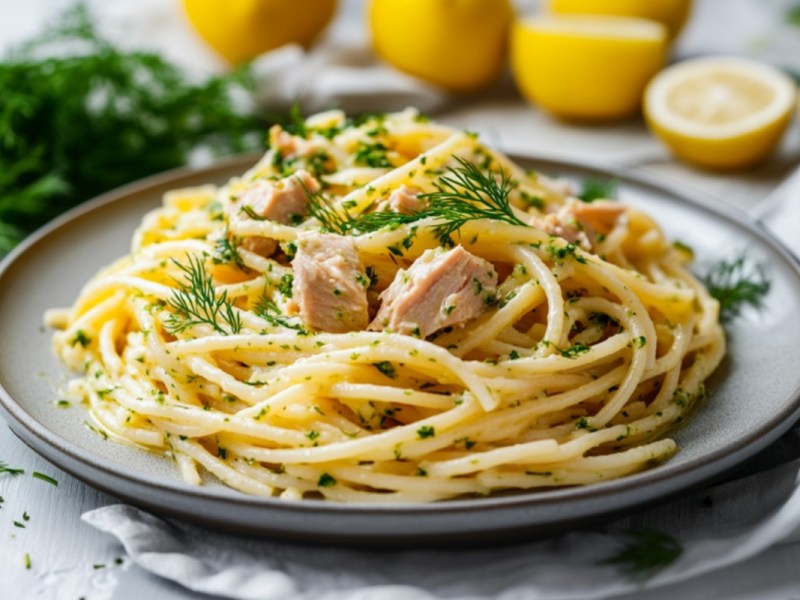 Ein Teller Thunfisch-Zitronen-Pasta mit Dill-Pesto. Im Hintergrund sind frische Zutaten zu sehen.