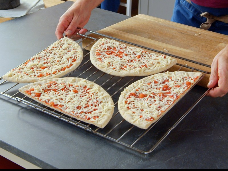 Zwei Pizzen auf einem Blech backen: Zwei Pizzen liegen angeschnitten auf einem Kuchengitter.