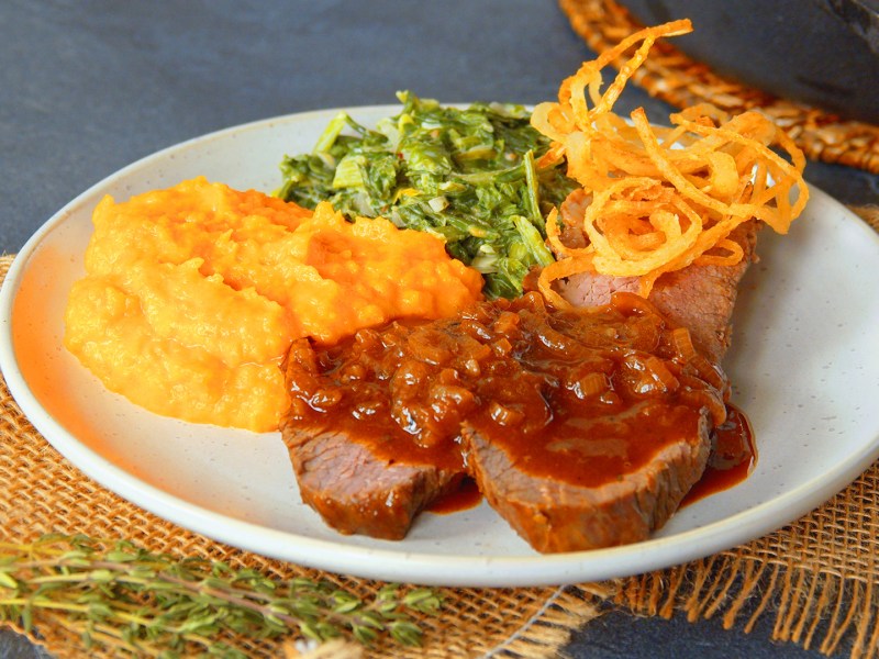 Zwiebelrostbraten mit KÃ¼rbispÃ¼ree und RÃ¶stzwiebeln auf einem Teller.