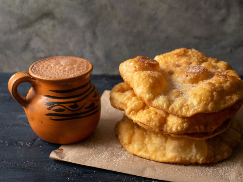 BuÃ±uelos: mexikanische Weihnachtskrapfen neben einer Tasse mexikanischer heiÃŸer Schokolade.