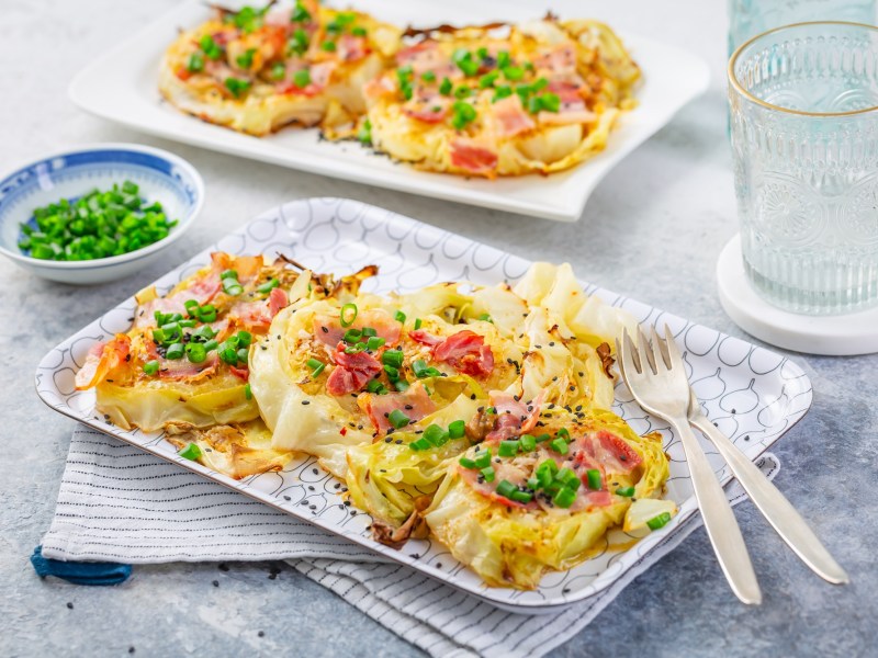 Zwei Servierplatten mit gebackenem WeiÃŸkohl mit Parmesan und Speck auf einem Tisch