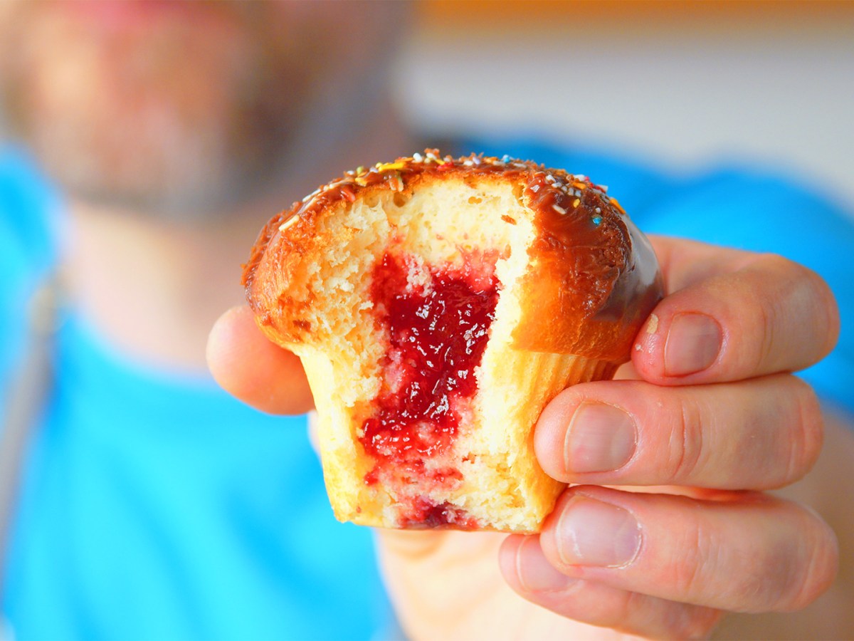 Ein halbierter Krapfen-Muffin aus dem Airfryer wird von einem Mann gehalten, den man unscharf im Hintergrund sieht.