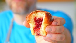 Ein halbierter Krapfen-Muffin aus dem Airfryer wird von einem Mann gehalten, den man unscharf im Hintergrund sieht.