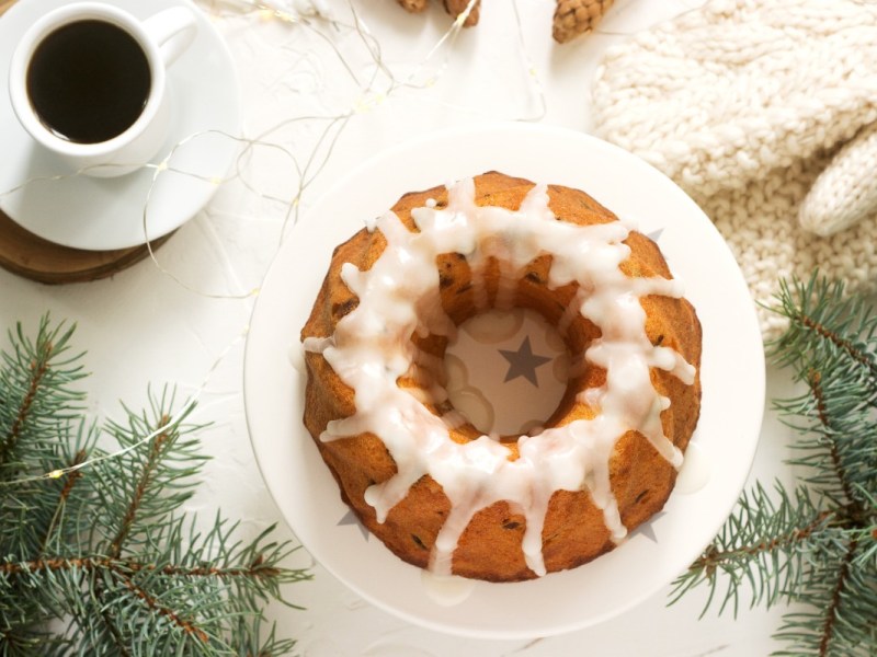 Ein Lebkuchen-Kuchen mit Zuxkerglasur in der Draufsicht. Drumherum liegt Weihnachtsdeko. Daneben steht eine Tasse Kaffee.