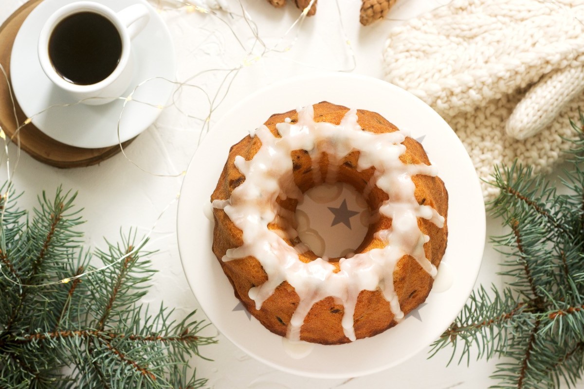 Ein Lebkuchen-Kuchen mit Zuxkerglasur in der Draufsicht. Drumherum liegt Weihnachtsdeko. Daneben steht eine Tasse Kaffee.