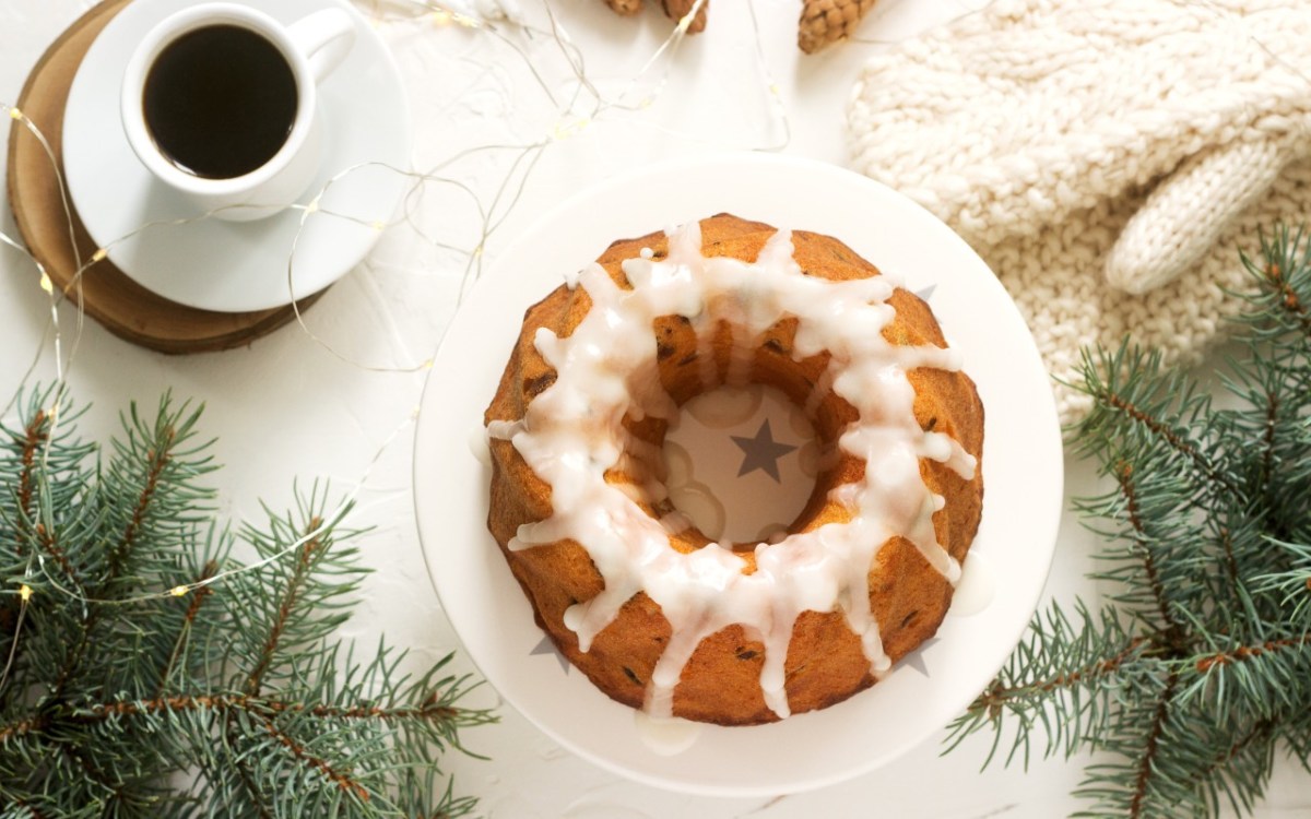 Ein Lebkuchen-Kuchen mit Zuxkerglasur in der Draufsicht. Drumherum liegt Weihnachtsdeko. Daneben steht eine Tasse Kaffee.