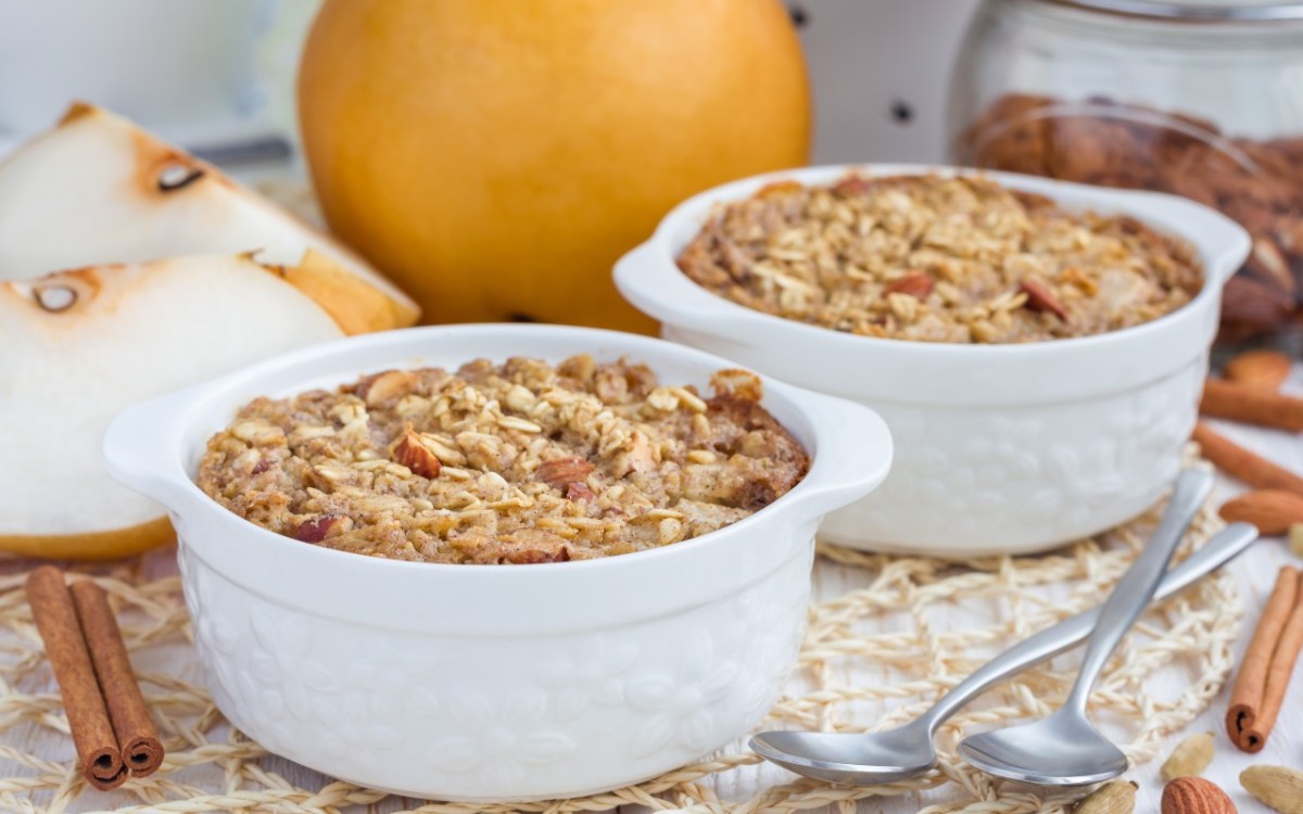 Zwei kleine FÃ¶rmchen mit Ofen-Porridge. Im Hintergrund liegen frische Birnen.