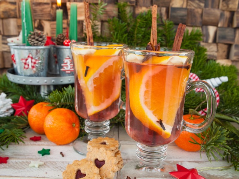 2 Glastassen mit Orangenpunsch. Der Hintergrund ist weihnachtlich dekoriert.