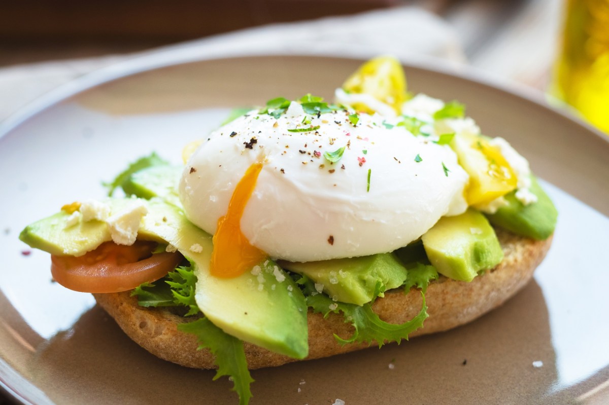 Ein Teller mit einem halben BrÃ¶tchen, auf dem Avocado und ein pochiertes Ei aus der HeiÃŸluftfritteuse liegen. Nahaufnahme.