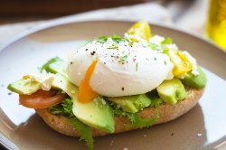 Ein Teller mit einem halben Brötchen, auf dem Avocado und ein pochiertes Ei aus der Heißluftfritteuse liegen. Nahaufnahme.