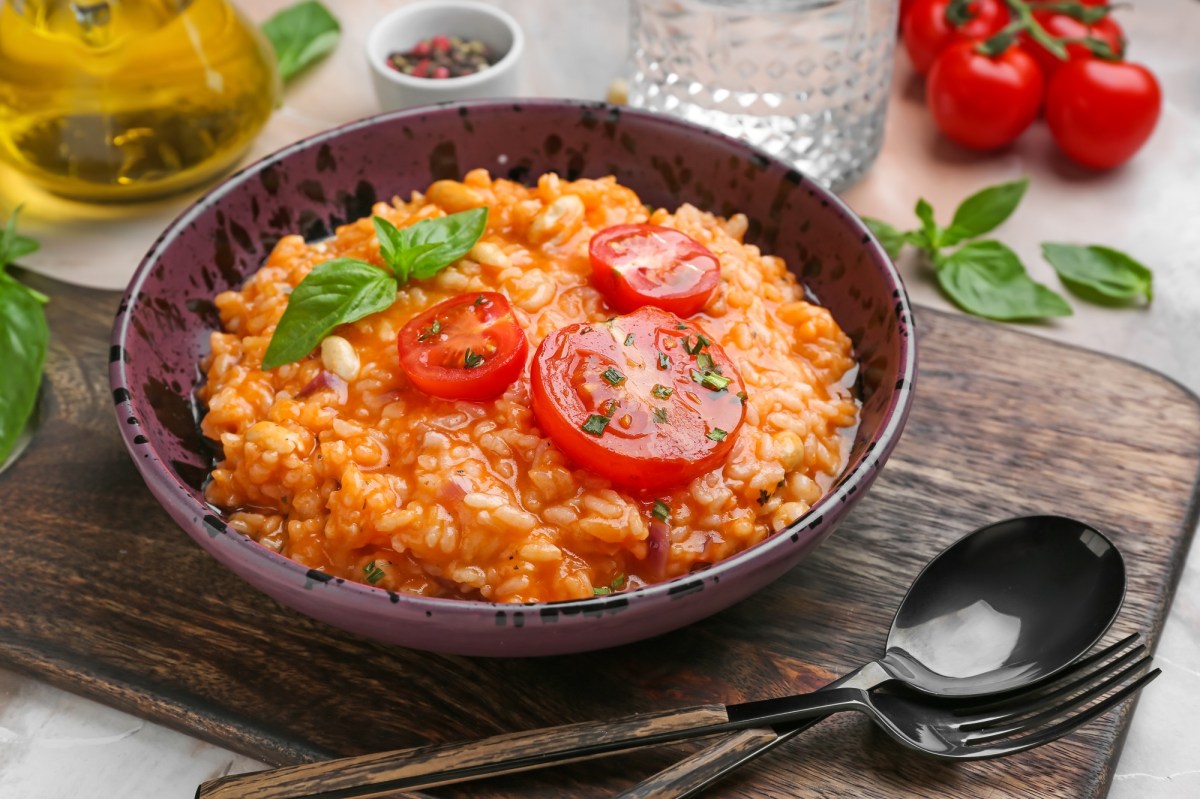 Italienischer Tomatenreis mit Bohnen in einer Schüssel, garniert mit Tomatenscheiben und Basilikum. Drumherum einige Zutaten.