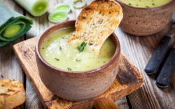 Eine Schale mit veganer Lauch-Pastinaken-Suppe, in der ein Stück kross gebackenes Brot steckt.