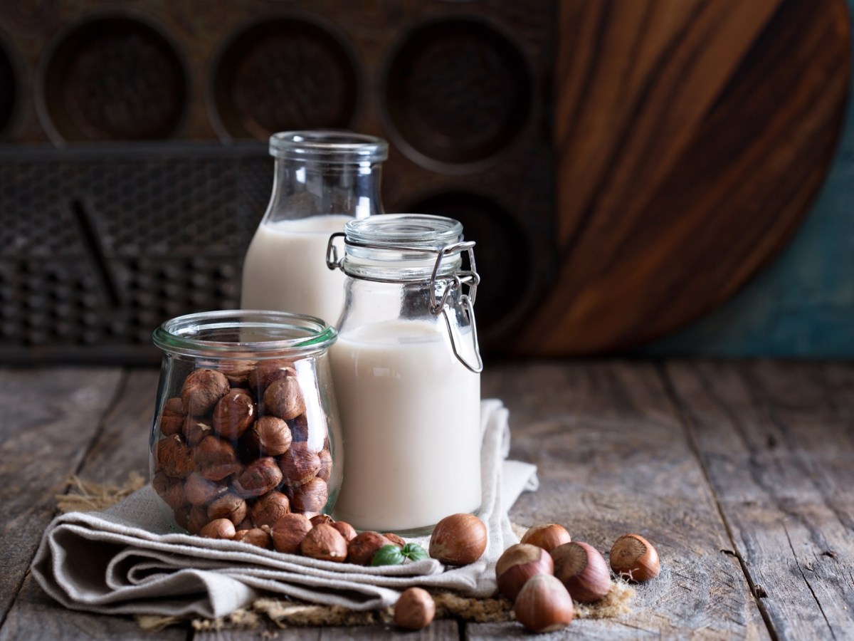 Nussmilch selbst machen: zwei Flaschen Haselnussmilch, davor Haselnüsse.