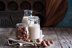 Nussmilch selbst machen: zwei Flaschen Haselnussmilch, davor Haselnüsse.