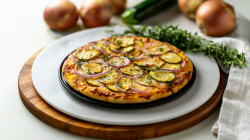 Raclette-Pizza mit Zucchini, Zwiebel und Kartoffeln belegt und mit Kräutern bestreut. Drumherum einige Zutaten.