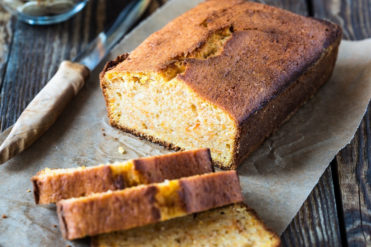 Veganer Chai-Kuchen liegt angeschnitten auf einem StÃ¼ck Backpapier auf einem dunklen Holztisch.