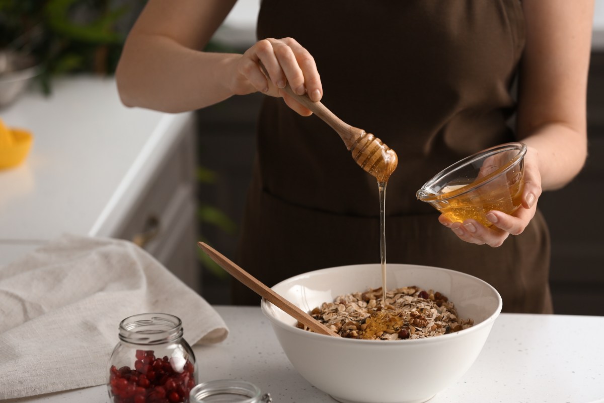 Eine Frau süßt ihr Müsli mit veganem Honig, man sieht nur ihre Hände und ihren Oberkörper.