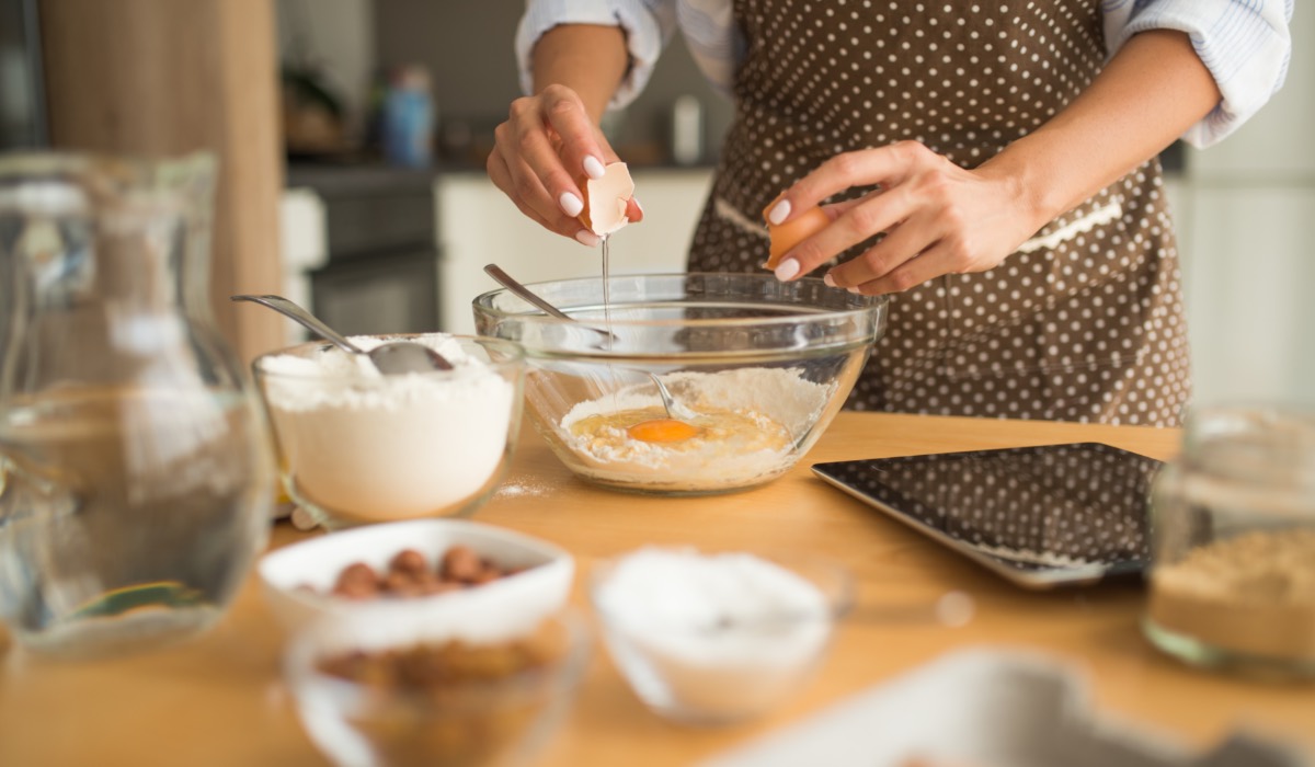 Tipps Backen: Eine Frau schlägt Eier in eine Schüssel auf. Drumherum stehen Backzutaten.