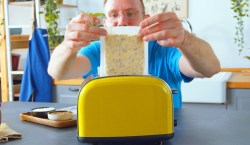 Fetabrotteig für ein Feta-Sandwich wird zwischen zwei Backpapieren in einen Toaster gegeben.