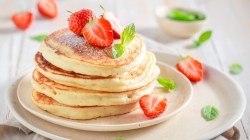 Ein Stapel Pancakes mit Buttermilch auf einem Teller, die mit Erdbeeren dekoriert sind.