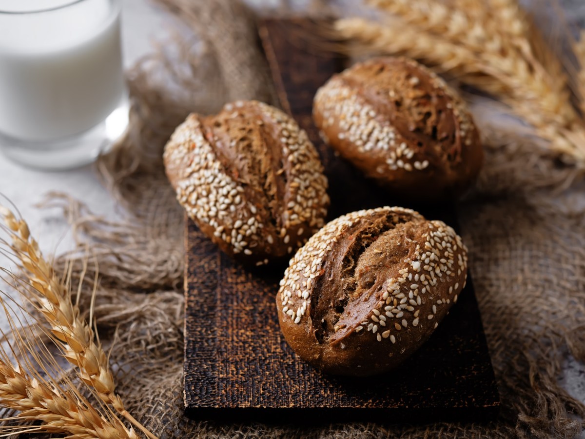 Drei Roggenbrötchen, garniert mit Sesam, auf einem Holzbrett.