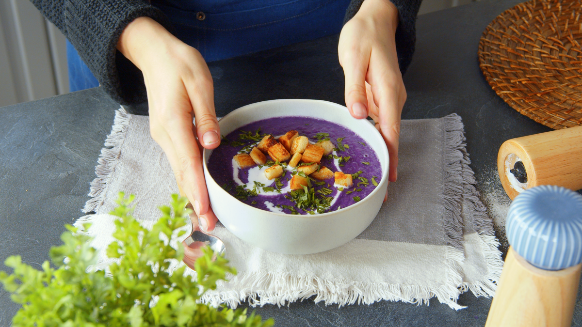 Eine Köchin präsentiert eine Schale mit lilafarbener Rotkohl-Kartoffel-Suppe.