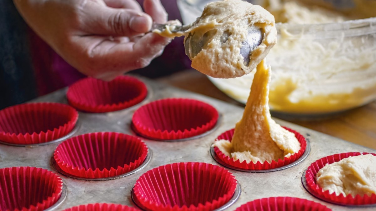 Backen mit Silikonformen: Jemand füllt Teig in eine Silikon-Muffinform.