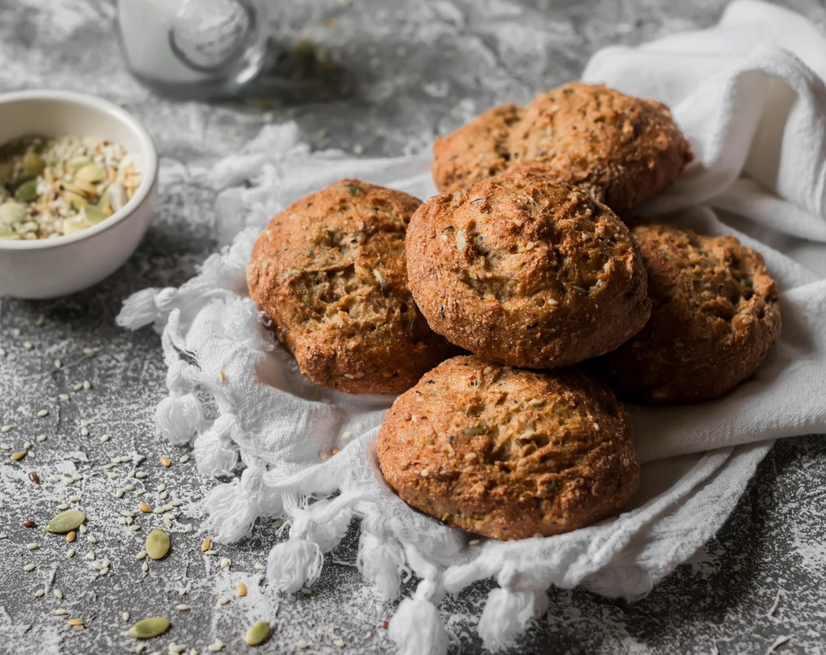 Mehrere Vollkornbrötchen mit Saaten auf einem hellen Tuch.